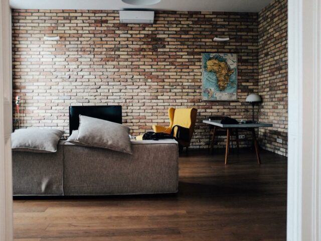 Sala de estar com parede de tijolo aparente, sofa cinza e piso de madeira
