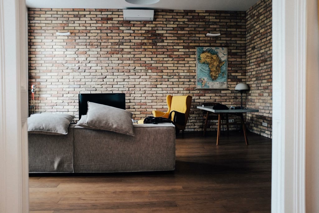 Sala de estar com parede de tijolo aparente, sofa cinza e piso de madeira